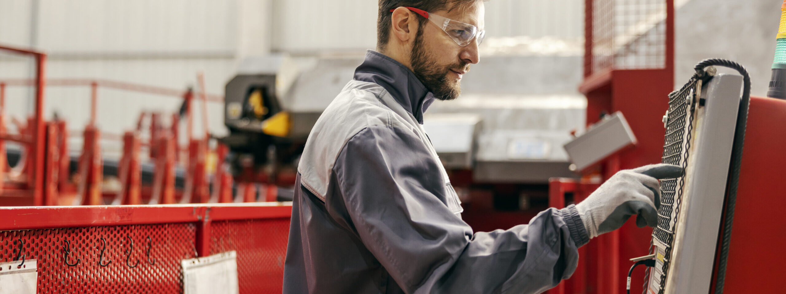 A heavy industry worker is managing machine and pressing buttons on dashboard while standing in facility.